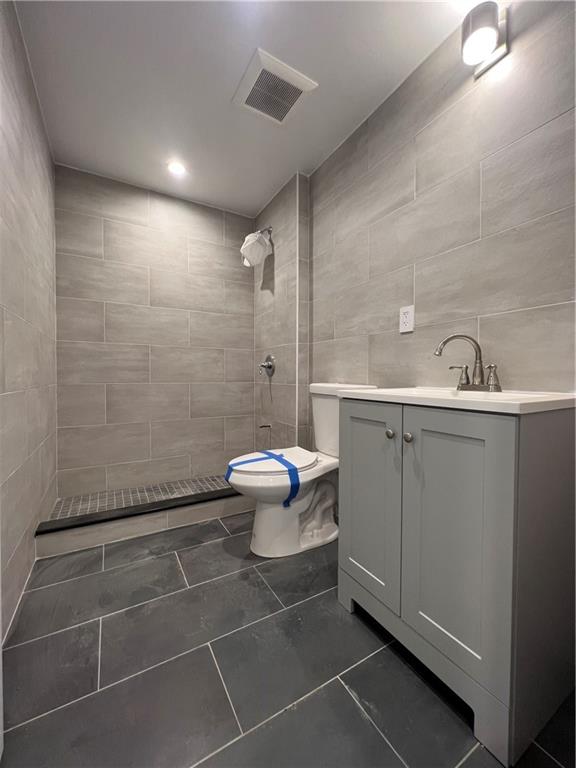 bathroom with a tile shower, vanity, tile walls, tile patterned flooring, and toilet