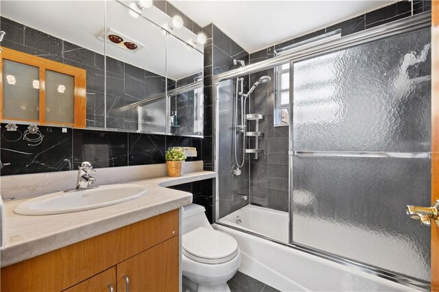 full bathroom featuring decorative backsplash, bath / shower combo with glass door, vanity, tile walls, and toilet