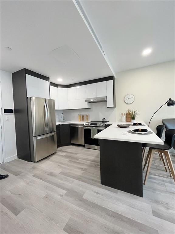 kitchen featuring a kitchen bar, appliances with stainless steel finishes, light wood-type flooring, kitchen peninsula, and white cabinetry