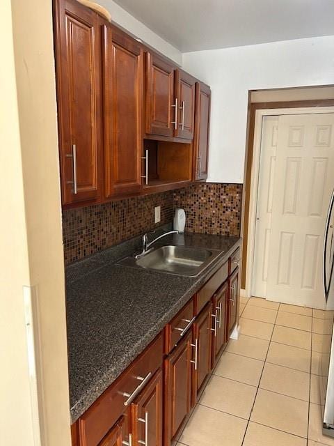 kitchen featuring light tile patterned floors, backsplash, dark stone countertops, and sink