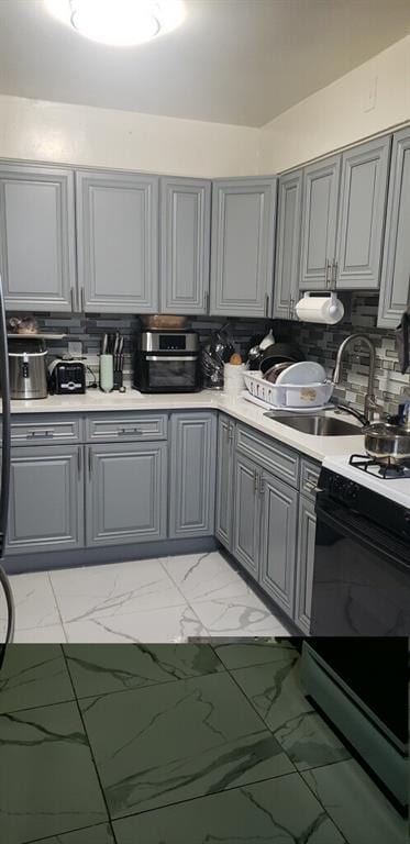 kitchen with gray cabinets, gas range oven, decorative backsplash, marble finish floor, and a sink