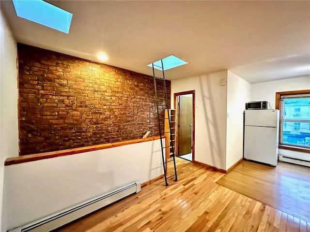 interior space featuring baseboard heating, a skylight, brick wall, and hardwood / wood-style flooring