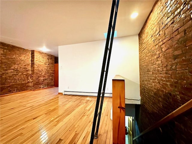 stairs with hardwood / wood-style floors, a baseboard heating unit, and brick wall