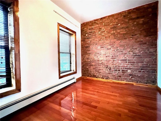 empty room with baseboard heating, wood-type flooring, and brick wall