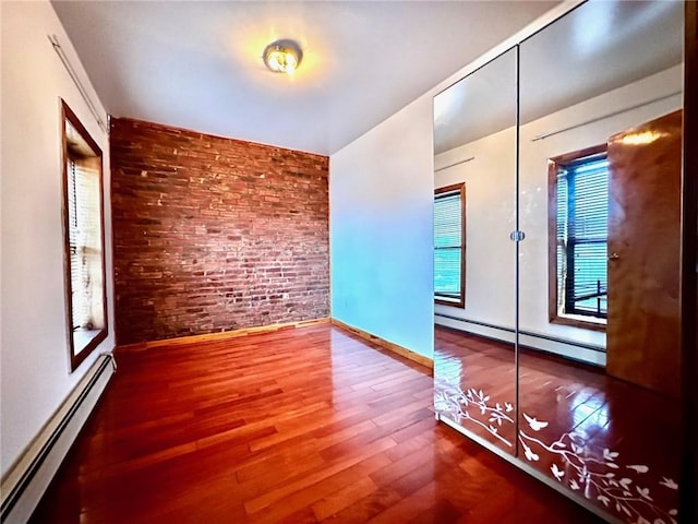 empty room with a baseboard radiator, brick wall, and wood-type flooring