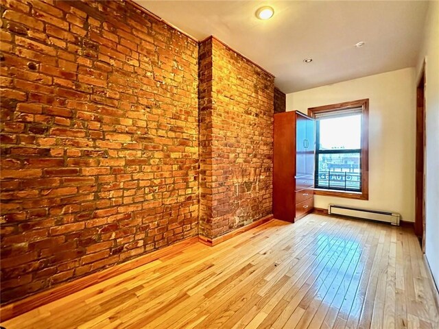 spare room featuring a baseboard radiator, light hardwood / wood-style flooring, and brick wall