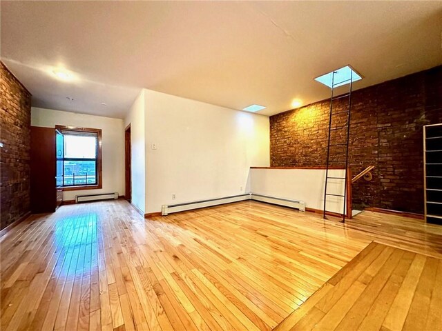 unfurnished room featuring a skylight, hardwood / wood-style floors, a baseboard radiator, and brick wall