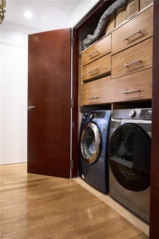 washroom with crown molding, washing machine and dryer, and light hardwood / wood-style floors