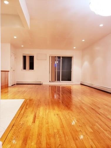 unfurnished room featuring a baseboard heating unit and hardwood / wood-style flooring