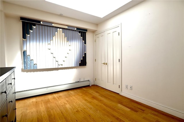 unfurnished bedroom with a closet, light wood-type flooring, and a baseboard heating unit