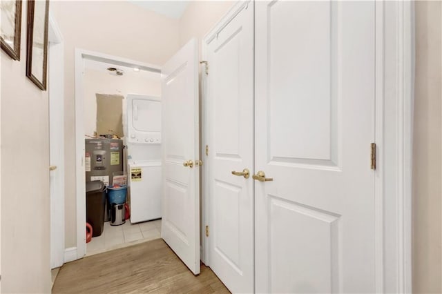 corridor with light hardwood / wood-style floors, stacked washer / drying machine, and water heater