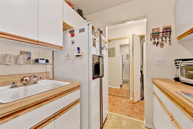 kitchen with light parquet floors, white cabinetry, white refrigerator with ice dispenser, and sink