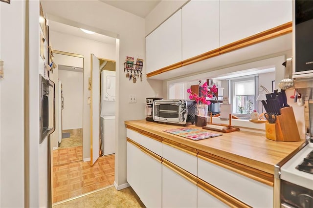 kitchen with white cabinetry, wood counters, stacked washer and clothes dryer, and light parquet floors