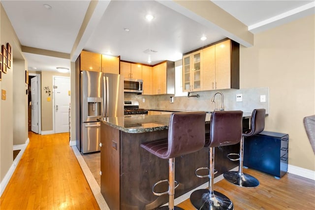 kitchen with a breakfast bar, light wood-type flooring, stainless steel appliances, backsplash, and light brown cabinetry