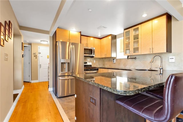 kitchen featuring dark stone counters, light wood-type flooring, sink, a kitchen bar, and stainless steel appliances