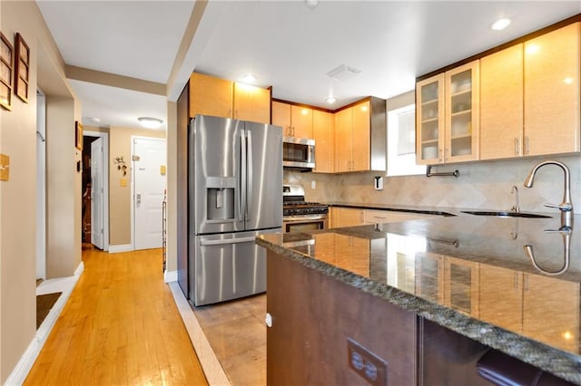 kitchen with sink, tasteful backsplash, appliances with stainless steel finishes, dark stone counters, and light hardwood / wood-style floors