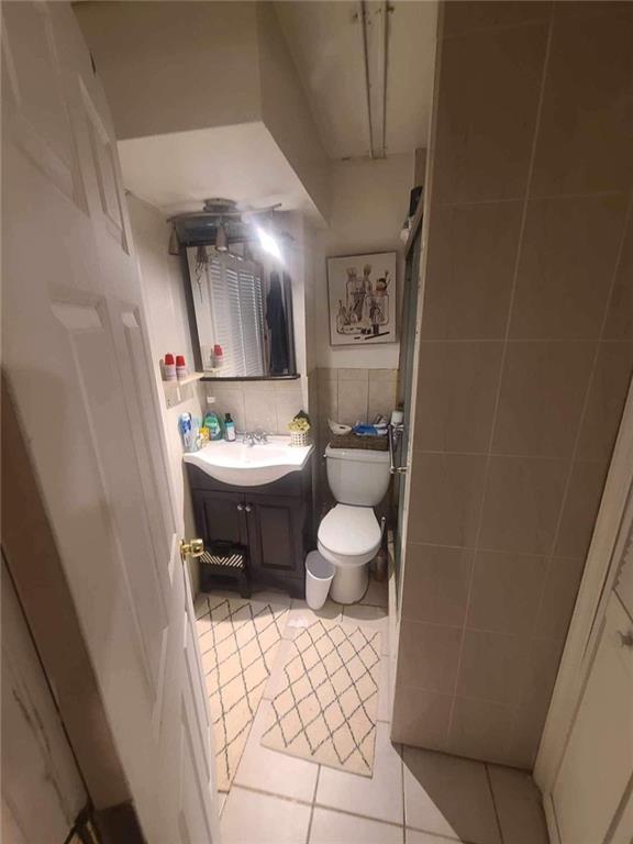 bathroom featuring tile patterned flooring, vanity, tile walls, and toilet