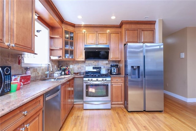 kitchen with sink, light hardwood / wood-style flooring, decorative backsplash, appliances with stainless steel finishes, and light stone counters