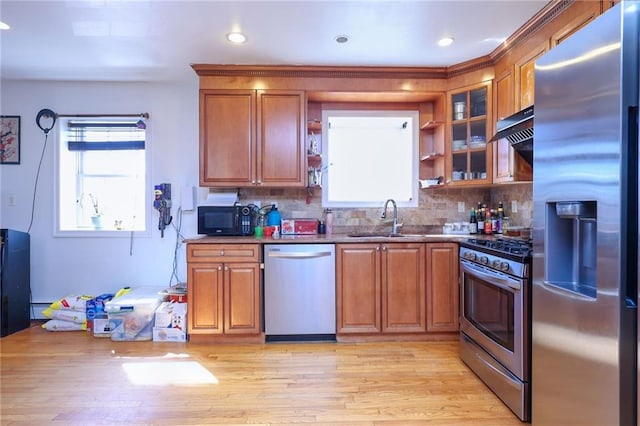 kitchen with a sink, under cabinet range hood, decorative backsplash, brown cabinetry, and appliances with stainless steel finishes
