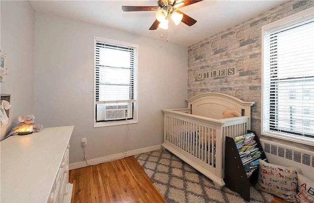 bedroom with multiple windows, radiator, wood finished floors, and baseboards