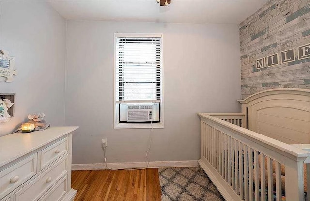 bedroom featuring baseboards, cooling unit, a crib, and light wood-style floors