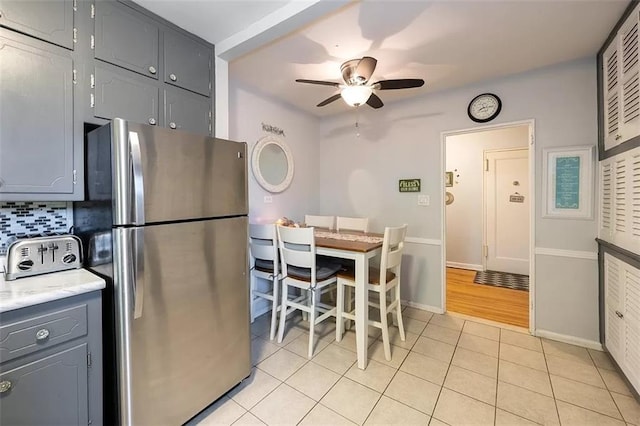 kitchen featuring light tile patterned floors, freestanding refrigerator, gray cabinetry, light countertops, and tasteful backsplash