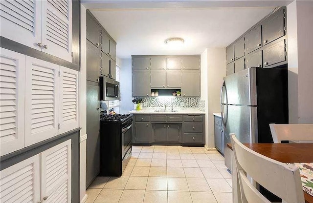 kitchen with a sink, light tile patterned flooring, appliances with stainless steel finishes, and gray cabinetry