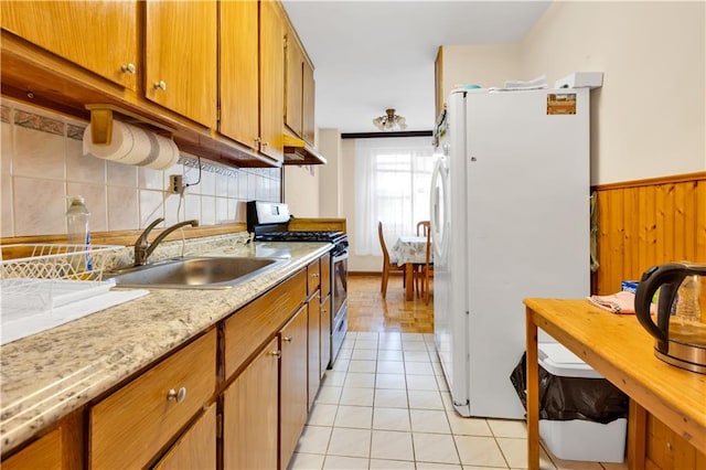 kitchen featuring sink, wooden walls, stainless steel gas range oven, white fridge, and light tile patterned floors