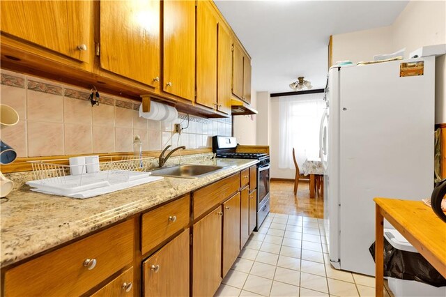 kitchen featuring decorative backsplash, stainless steel gas range, sink, light tile patterned floors, and white fridge