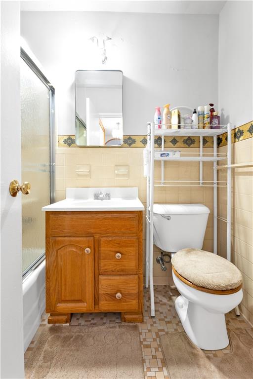 full bathroom featuring tile walls, vanity, bath / shower combo with glass door, and toilet