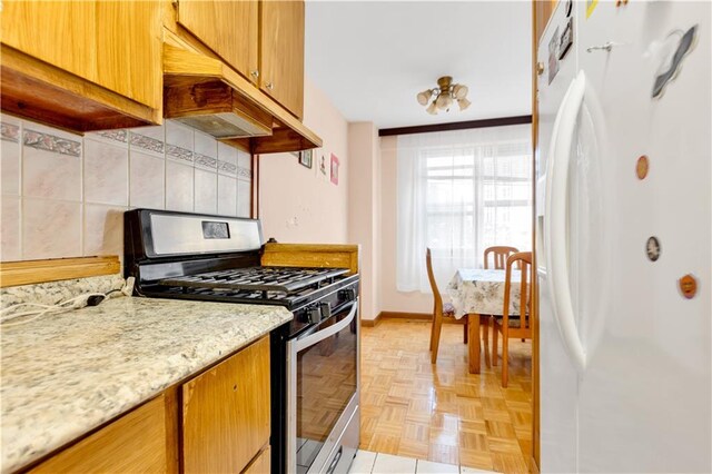 kitchen with light parquet flooring, stainless steel range with gas stovetop, white fridge, light stone counters, and decorative backsplash