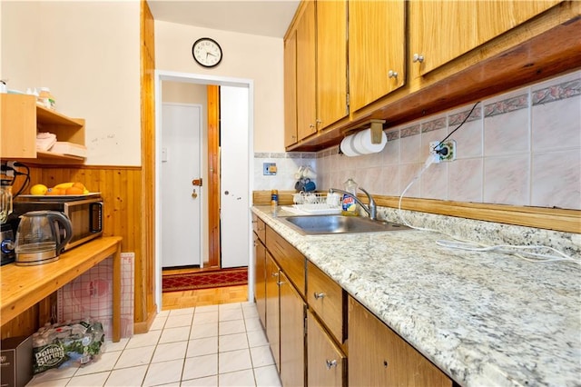 kitchen with decorative backsplash, sink, light stone countertops, light tile patterned floors, and wood walls