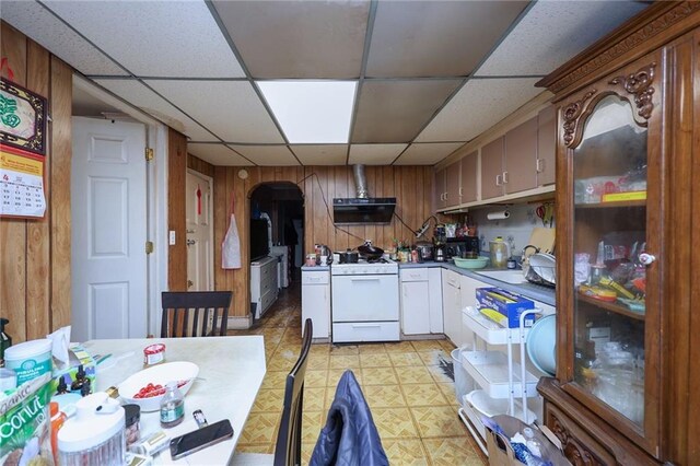 kitchen with a paneled ceiling, wood walls, sink, white gas range oven, and extractor fan