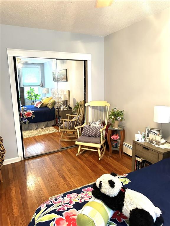 bedroom with a textured ceiling, baseboard heating, wood finished floors, and baseboards