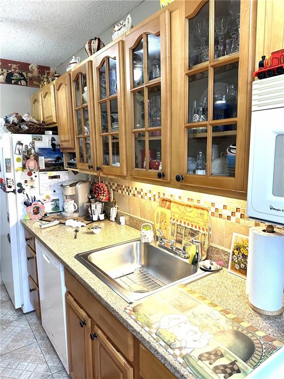 kitchen featuring sink, white appliances, light stone countertops, and a textured ceiling