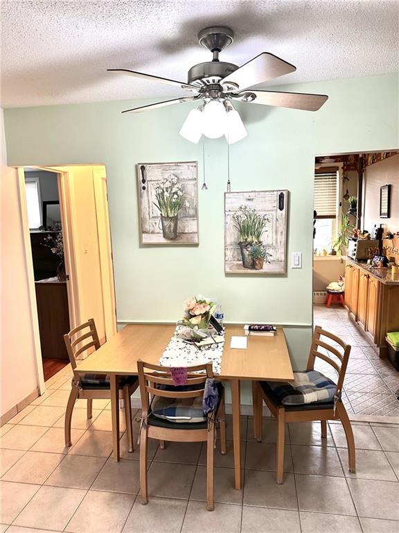 dining area with light tile patterned flooring, ceiling fan, and a textured ceiling