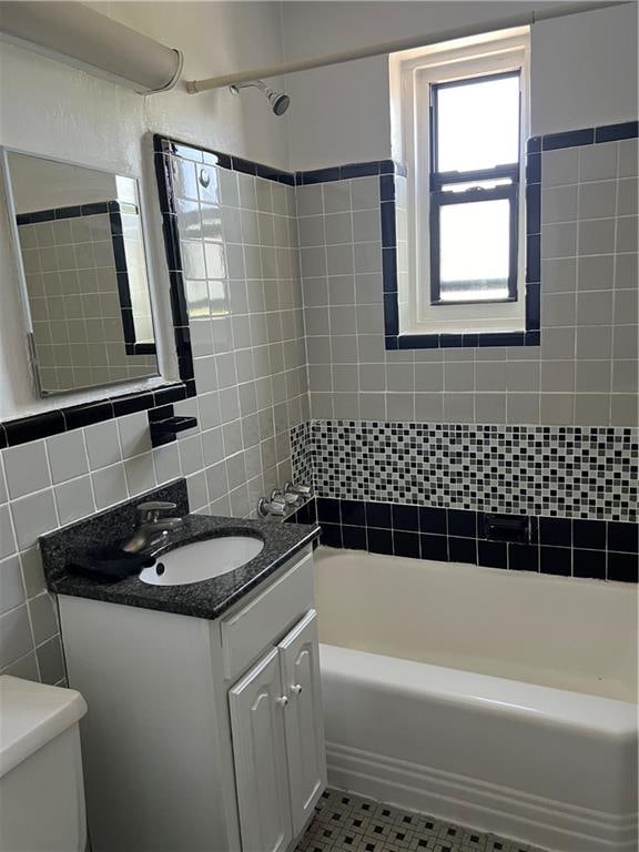 bathroom featuring toilet, vanity, shower / bathtub combination, tile patterned floors, and tile walls