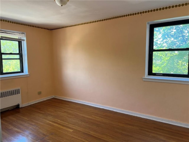 unfurnished room with radiator, baseboards, and wood finished floors