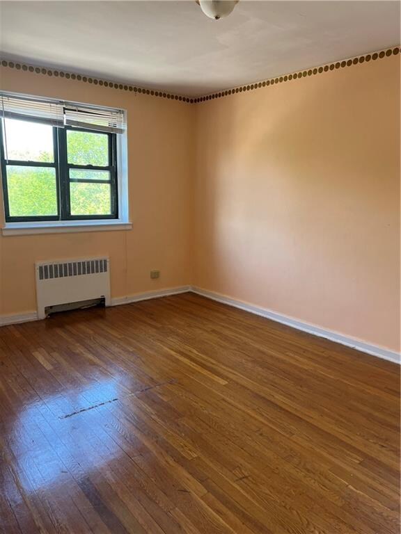 spare room featuring radiator heating unit and hardwood / wood-style floors