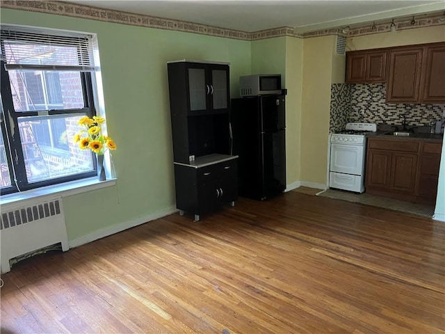 kitchen featuring light wood finished floors, radiator heating unit, freestanding refrigerator, stainless steel microwave, and white gas range