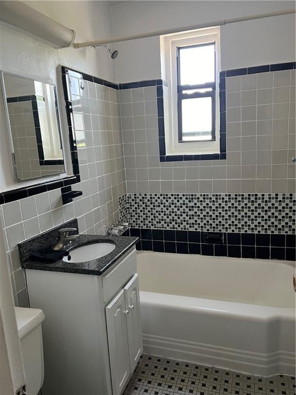 full bathroom with tile walls, tile patterned flooring, tiled shower / bath combo, vanity, and toilet