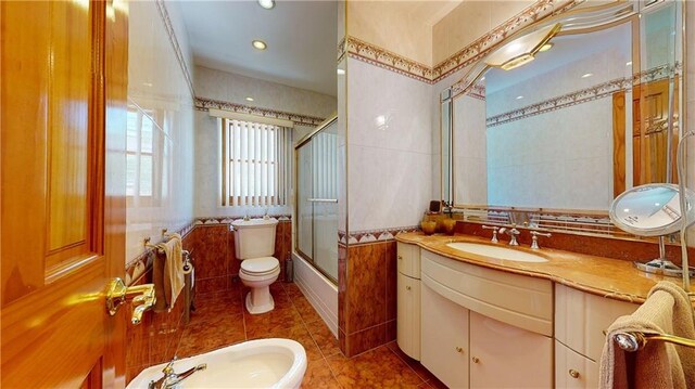 full bathroom featuring vanity, a bidet, combined bath / shower with glass door, tile patterned flooring, and toilet