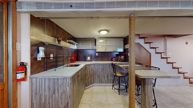 kitchen with backsplash, light tile patterned flooring, kitchen peninsula, and sink