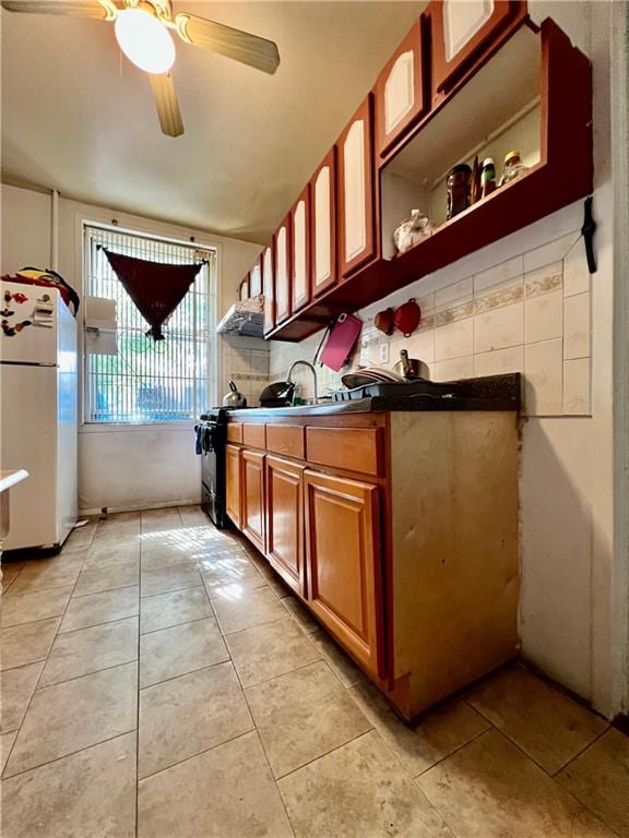 kitchen featuring ceiling fan, sink, light tile patterned floors, white refrigerator, and black range