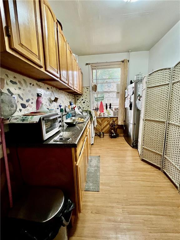 kitchen with decorative backsplash, stainless steel fridge, dark stone counters, and light hardwood / wood-style flooring