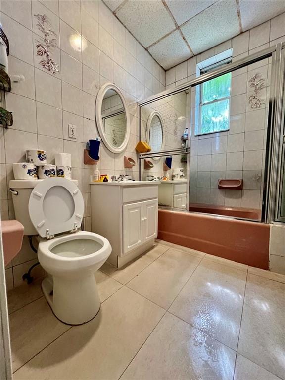 full bathroom featuring a paneled ceiling, vanity, toilet, enclosed tub / shower combo, and tile walls