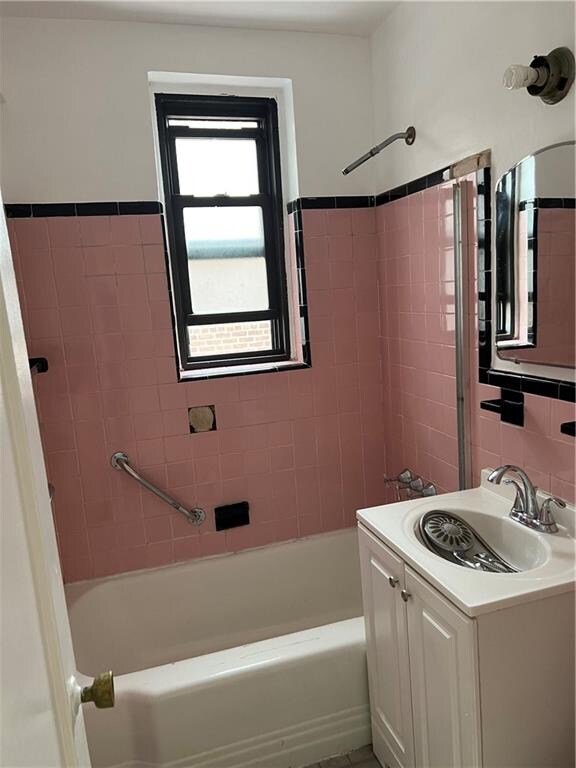 bathroom featuring tiled shower / bath combo, vanity, and tile walls