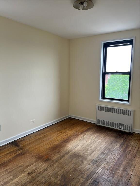 unfurnished room featuring radiator and dark wood-type flooring