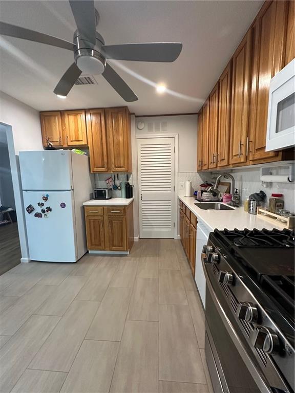 kitchen with brown cabinets, white appliances, light countertops, and a sink