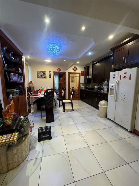 kitchen featuring white refrigerator with ice dispenser, dark brown cabinetry, and a tray ceiling